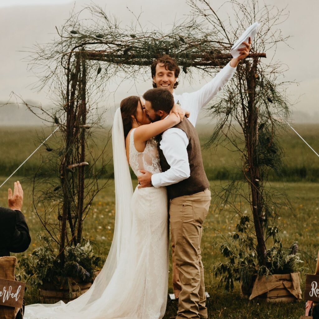bride and groom kissing in front of stick arch at ceremony with mountains behind them